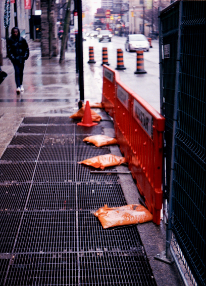Orange sandbags line an orange hazard fence along a subway grate.