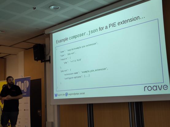 James Titcumb in front of a projector slide showing an example `composer.json` with extension dependencies (and configuration flags thereof) declared.