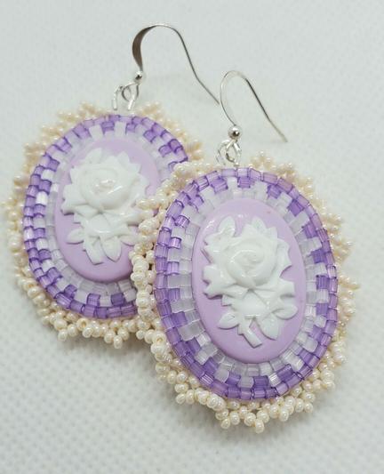 an elegant pair of beaded earrings. the centerpiece is a white rose on a lavender background surrounded by clear, light purple, and pearlescent beads to accentuate.