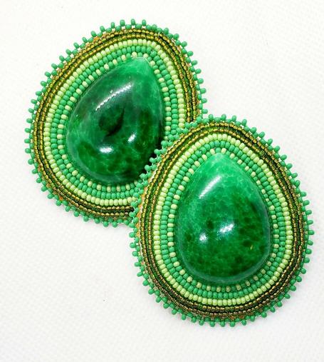 a rich green teardrop shaped beaded pair of earrings made by kiamichi. the centerpiece is a vibrant green stone which is surrounded by various colors of green beaded borders.