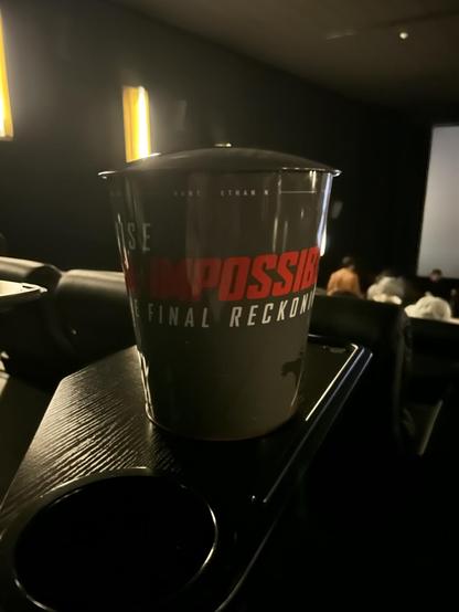 Ein Mission Impossible Popcorn-Becher aus grauem Blech mit roter und weißer Schrift.