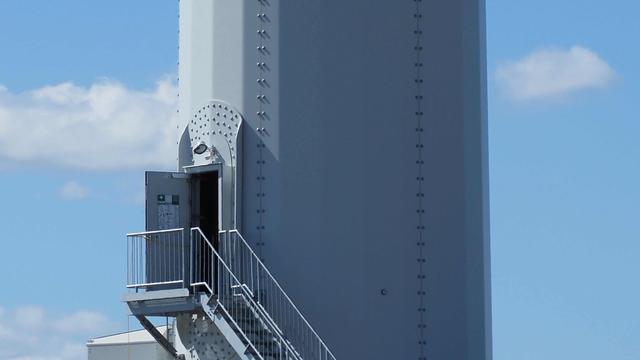Offene Tür an einem Windradmast. Himmel hellblau. Mast grau.