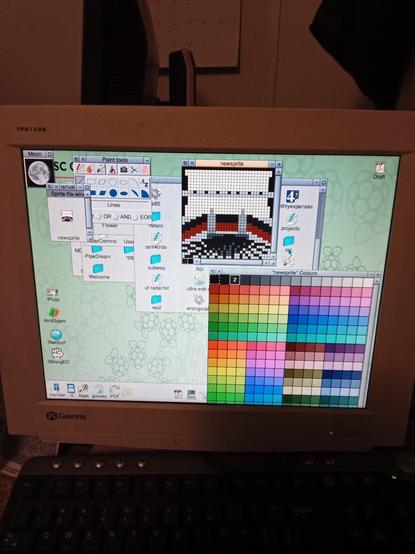 Risc OS screenshot. Editing a 256 color icon in the !paint app. Windows on screen include a color selector, tools, a view of the actual icon, and a 8 times zoomed image to actually edit. The icon shows a manual typewriter from the POV of a typer  roll of paper held down by a bar, with a black and red ribbon held against it and a spider-like mess of type bars beneath it.