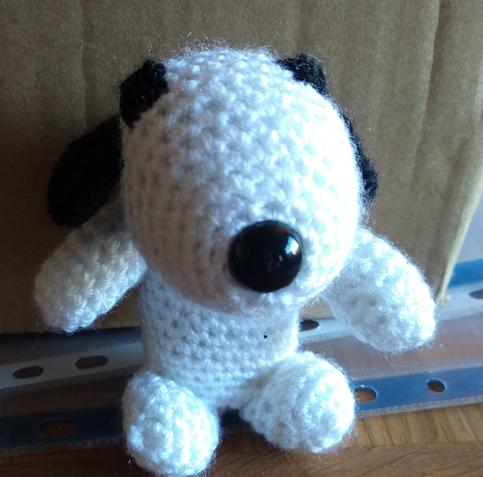Front view of a crochet snoopy with black nose, ears and eyes