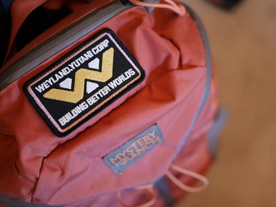 A Weyland Yutani Corp “Building Better Worlds” patch on my orange backpack.