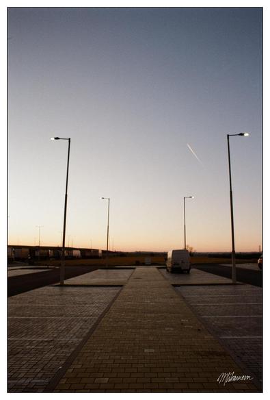 A photo of an evening sky above parkig lot with two streetlight posts and a contrail