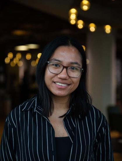 A photo of Jane looking happy, wearing glasses, a black shirt with white pinstripes and a black top underneath. Photo by Jasmijn de Lange.
