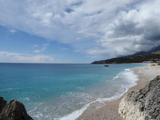 Low view of a long sandy beach beside turquoise water. Hills rise up from the beach.