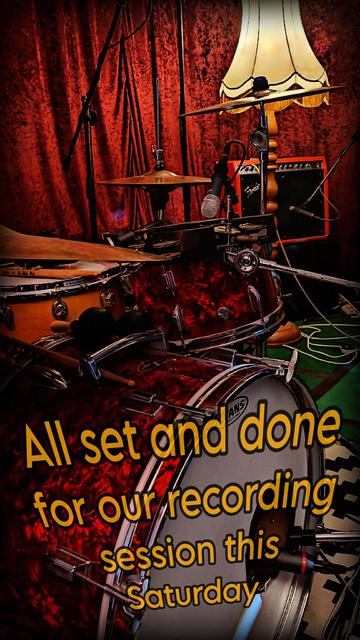 Zu sehen sind einige Mikrofone, ein rotes Drumset mit Bassdrum im Vordergrund, im Hintergrund sieht man eine alte Stehlampe und einen roten Fender-Amp. Im Hintergrund ein bordeauxfarbener Samtvorhang.