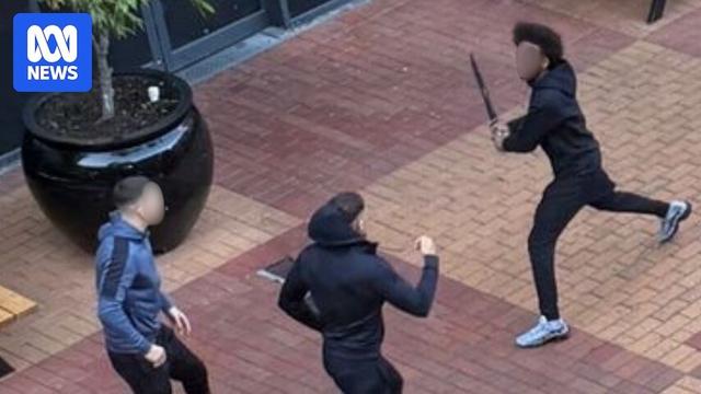 Two men stand back while another man wields a machete.