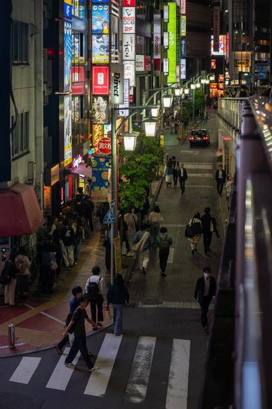 Night scene of a brightly lit narrow street. People are walking in the street.