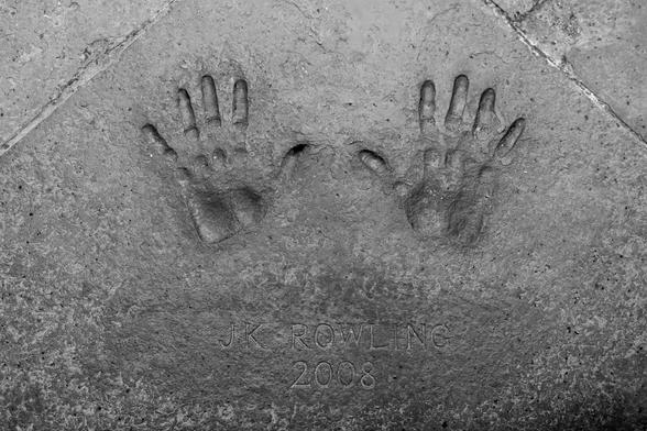 This image shows the handprints of J.K. Rowling embedded in stone or concrete. The handprints are accompanied by the inscription "J.K. Rowling 2008," indicating that these were made by the author in the year 2008. The image is in black and white, highlighting the textures and details of the handprints and the surface on which they are imprinted.
