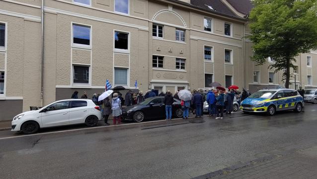 Menschenmenge vor einem mehrstöckige Wohnhaus. Ein Polizeiwagen spert die Fahrbahn ab.