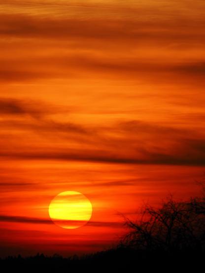 The sun sets and bathes the sky, which is covered in clouds, in a warm red colour.