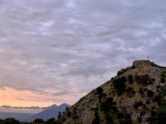 Castle on hill with fading orange light over mountains left of frame