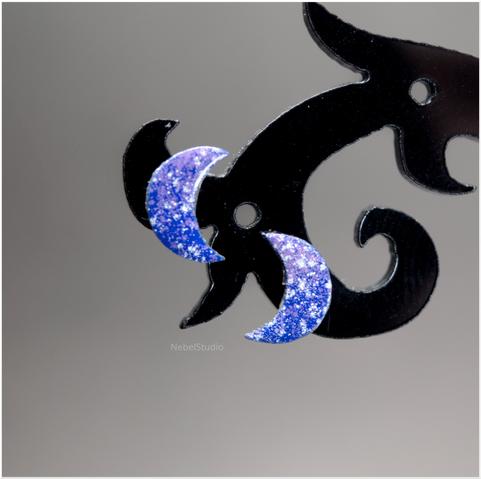 un par de pendientes minis cada uno en forma de media luna, de menos de 1cm de alto, esmaltados en tonos azules y violetas, con motitas blancas, como si fueran cielos estrellados.