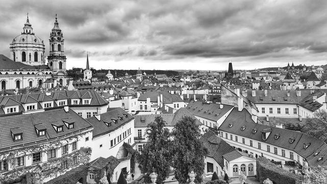 Schwarz-Weiß-Foto. Blick von einem Hügel über sehr viele Dächer und ein paar Türme. Der Himmel ist grau und wolkig.