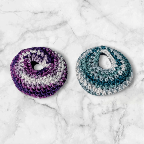 Purple ombre and teal ombre crochet fidget donuts on a marble background.