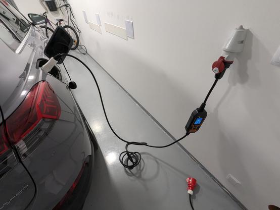 A photo from a garage. The charger is connected to a 3-phase plug and to a car.