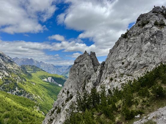 Rocky outcrops with person standing on top far right; green-clad valley left of frame