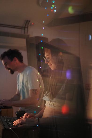 Two people doing live coding at their laptops. The image is distorted slightly due to the use of a triangular prism