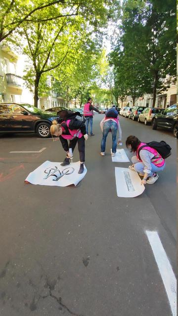 Ein Foto von einer Straße, auf der 4 Menschen in pinken Warnwesten tagsüber einen Radweg selbermachen. Mit Schablonen sprühen sie Fahrradwegmarkierungen und -symbole auf die Straße.