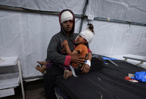 A wounded Palestinian sits while holding a child, at Al-Ahli Arab Baptist hospital.