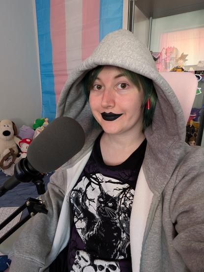 Revy wearing black lipstick and a big grey hoodie
She's near a microphone