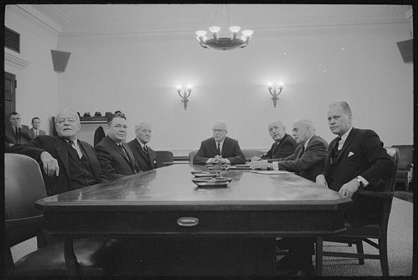The Warren Commission, which investigated the assassination of President John F. Kennedy, 1963, and which generated many conspiracy theories about the “deep state.” From left to right: former CIA Director Allen Dulles, Representative Hale Boggs, Senator John Cooper, Chief Justice Earl Warren, Senator Richard Russell, Chairman of the Council on Foreign Relations John McCloy, and Representative Gerald Ford ; B&W photo of seven men in suits sitting around a conference table