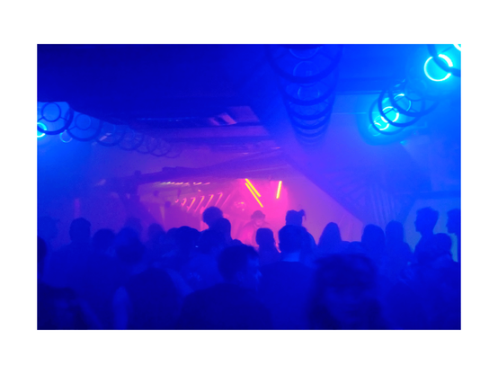 club situation, dj booth built from wooden structures with dancing people in front, in blue and pink light