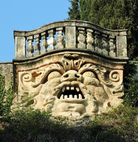 Estructura de roca tallada con forma de cara monstruosa bajo un balcón.