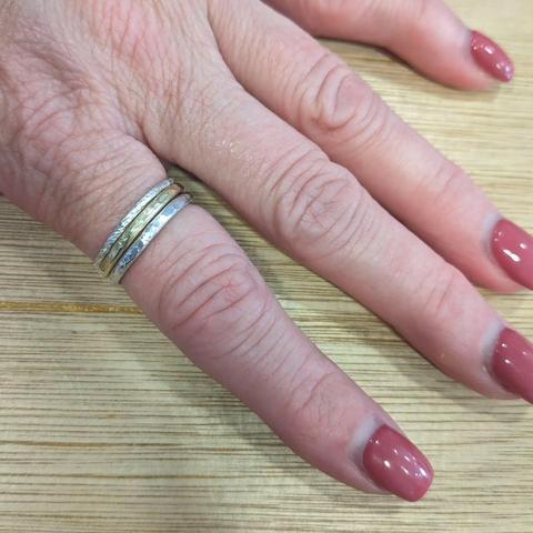 A hand laid out on a wooden table, wearing a set of three stacking rings on the index finger