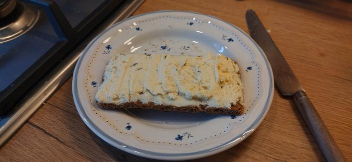 cheese smeared on a rectangular knäckebröd on a small plate. The cheese has been dried so it looks a bit crumbly.
