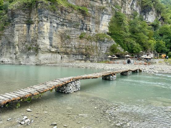 Makeshift bridge made from wood resting on gabions leading to bar on opposite bank