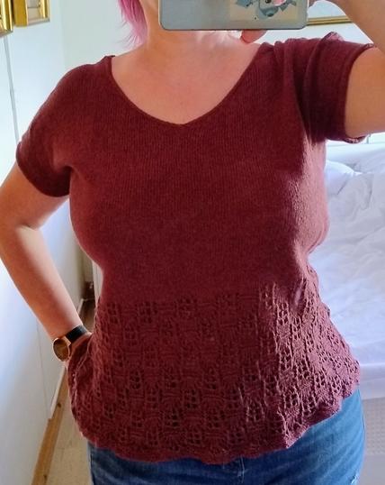 Headless woman wearing a knit shirt with a wide lace panel at the bottom in a dark wine red color.

She's taking a selfie in a mirror, her right hand up, holding a camera which is only partly visible. 

The view is from full front