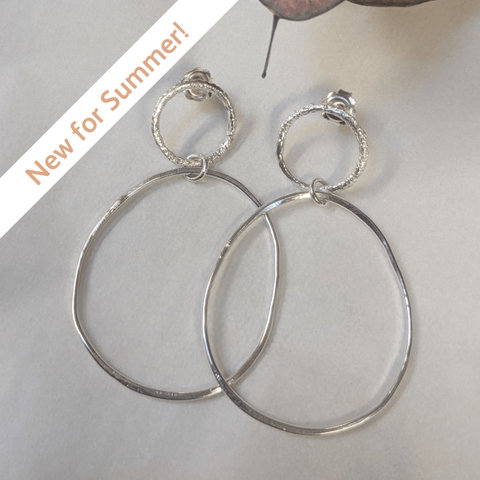 A pair of silver earrings, formed of a large oval-ish hoop connected by a jump ring to a smaller silver hoop
