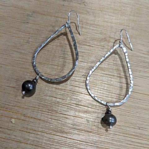 A pair of silver earrings formed of textured flat wire in a teardrop shape, decoratedd with a small bead