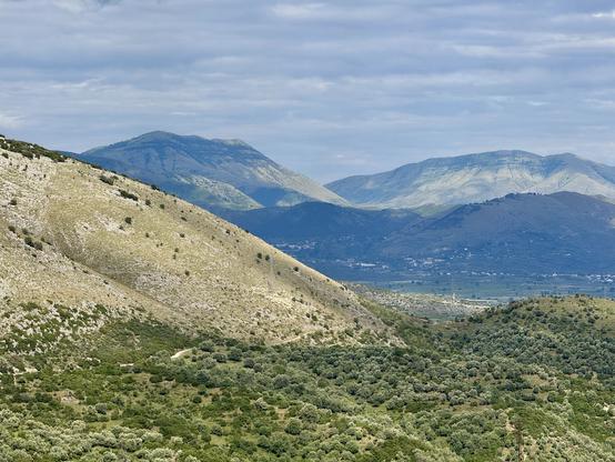 Scrub-clad hill, beyond which a plain & in distance a massif