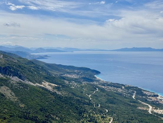 Green slopes lead down to developments on coast; Corfu on horizon right of frame