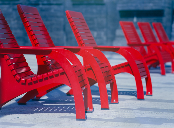 A row of bright red metal muskoka chairs lined up in a public space.