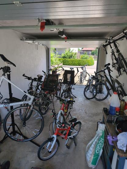 Blick durch eine Garage mit den Fahrrädern einer 5-köpfigen Familie.

- KTM Ebike mit Anhänger
- 2x Hase Pino Tandem (eins davon geliehen)
- KTM Stadtrad mit FollowMe um ein Kinderrad zu ziehen
- Woom 3, 4 und 5
- Orbea Jugendrad
- Müsing und Canondale Rennrad
- Stevens Gravelbike