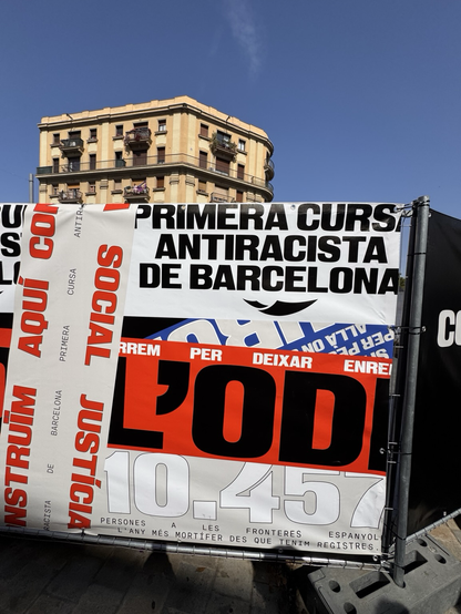 Signs at the finish line of the Primera Cursa Antiracista de Barcelona, including showing the thousands of deaths of migrants trying to cross the sea