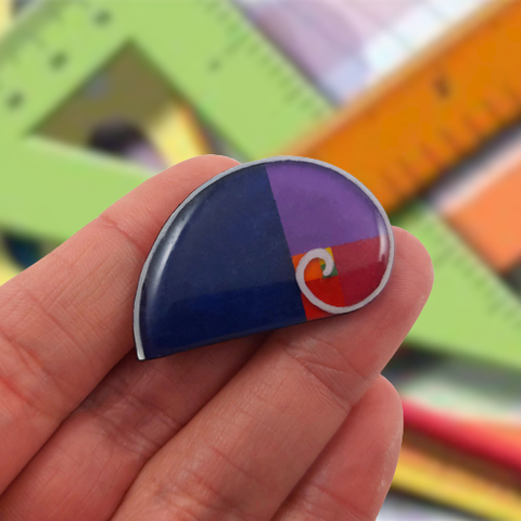 Broche éco-responsable en forme de spirale de Fibonacci.
La perle est réalisée en CD recyclé, découpée et peinte à la main, puis recouverte de résine époxy.
Les couleurs sont personnalisables.