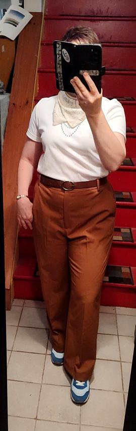 White T with sleeves cuffed. Mocha trousers and belt. Blue, beige, and pale yellow neckerchief tied backwards, over a blue bead necklace. Blue Adidas knock-offs.