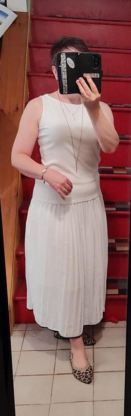 Sleeveless white knit top, billowy white skirt with black edging. Leopard print flats, long gold chain layer necklace.