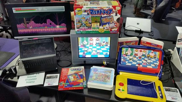 A travelling Japanese Sega Pico exhibit with several software titles about. Onscreen is a Hello Kitty game. Above the TV is a special hardware accessory for the Pico. Left is an indie game also on display.