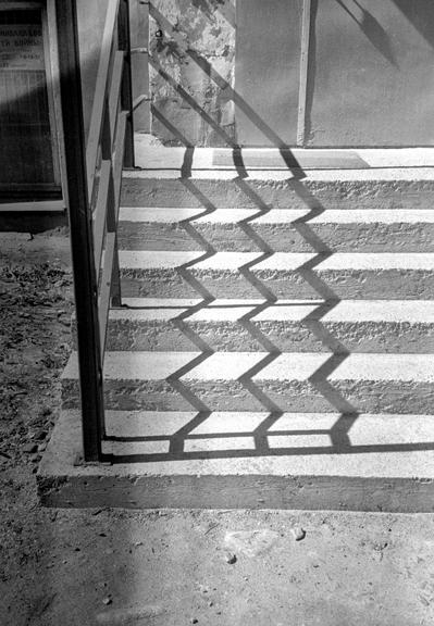 Monochrome photo. The photo shows a porch with the shadow of the railing falling on it in zigzags.
