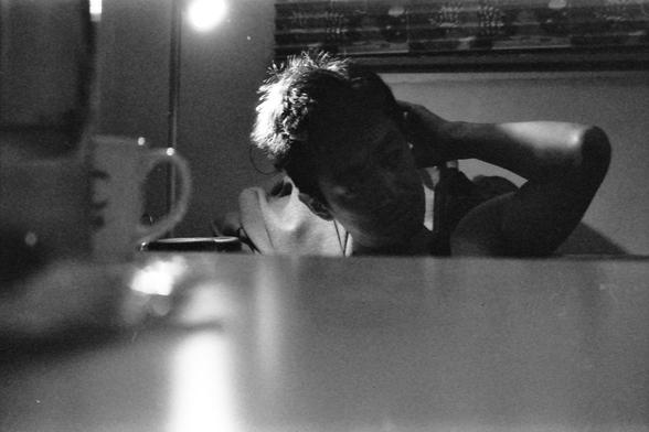 Ilford FP4 E.I. 64

**English Alt Text:**
- Description: A black-and-white photograph of a person sitting at a table. The person is leaning forward with their head resting on their hand, appearing to be in deep thought or possibly tired. There is a cup on the table in front of them, and the background is slightly blurred, focusing attention on the person. The lighting is soft, creating a reflective surface on the table.

**Chinese Alt Text:**
- 描述：一张黑白照片，照片中一个人坐在桌子旁。这个人向前倾身，头靠在手上，看起来像是在深思或者有些疲惫。桌子上有一个杯子，背景稍微模糊，将注意力集中在人物身上。灯光柔和，在桌面上形成了反光。