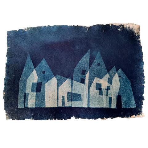 The image is a cyanotype, or blue print, on textured paper. It depicts lighter blue and white houses on a blue background, aligned horizontally but overlapping each other.