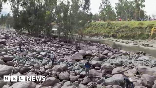 A wide shot of bolders and people looking at the aftermath of a landslide in Peru
